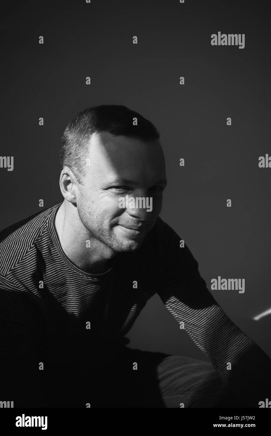 Studio artistique sombre portrait de jeune adulte homme assis dans l'ombre sous les rayons du soleil sur son visage, photo noir et blanc vertical Banque D'Images