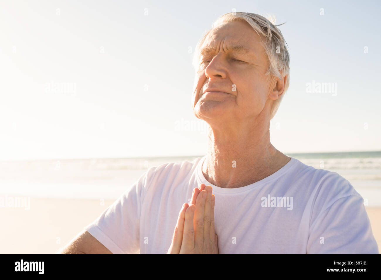 Senior homme avec les yeux fermé en position de prière at beach Banque D'Images