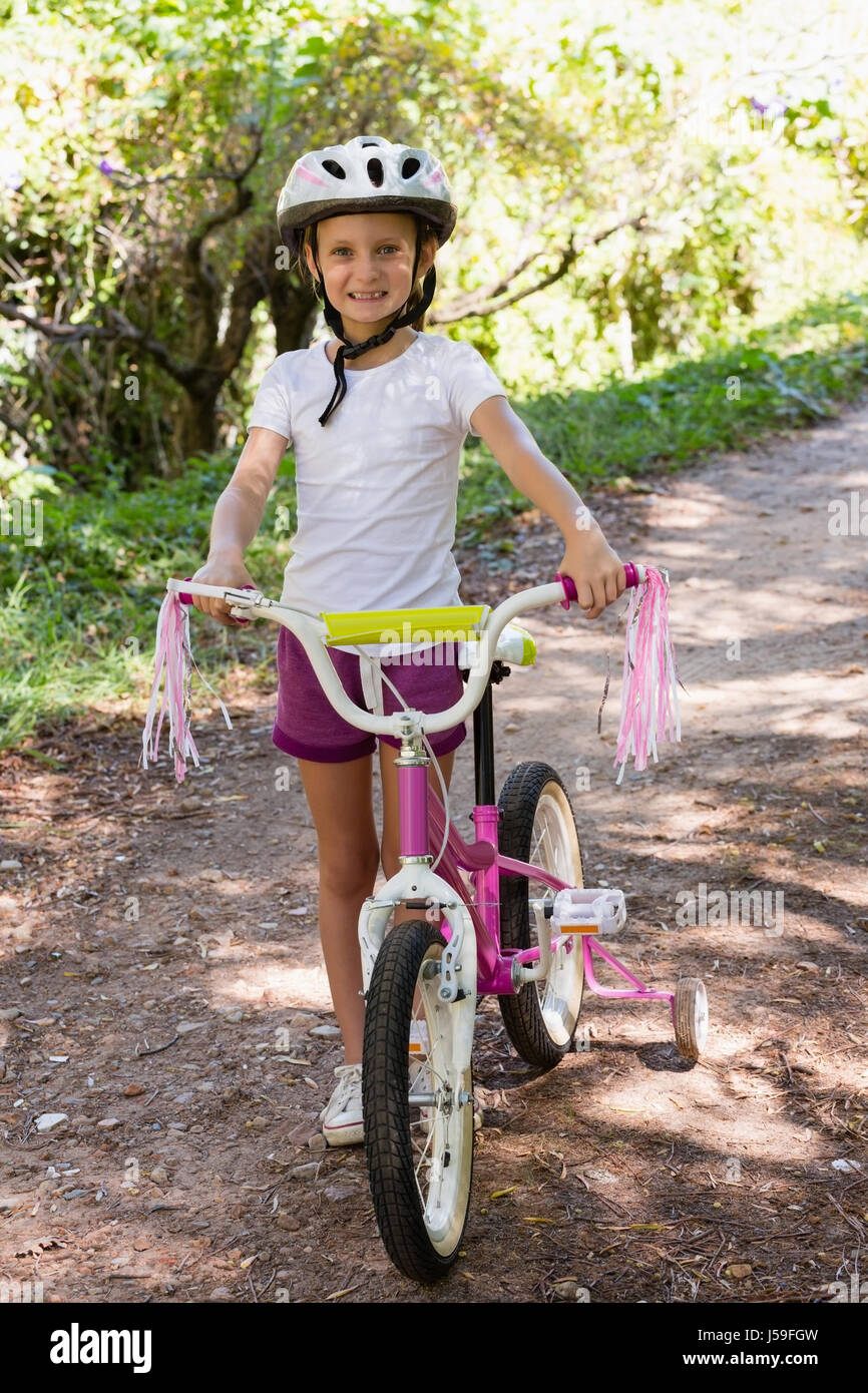 Portrait of smiling girl du vélo dans la forêt lors d'une journée ensoleillée Banque D'Images