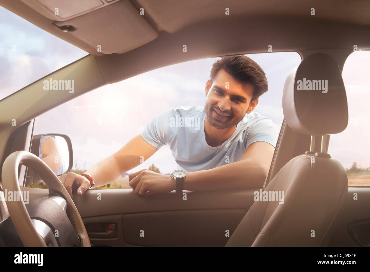 Smiling young man leaning on car window Banque D'Images