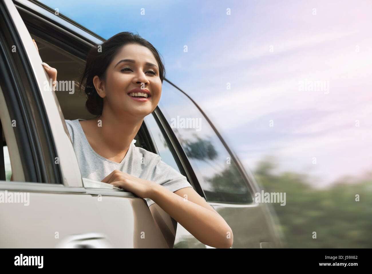 Smiling young woman peeking from car window Banque D'Images