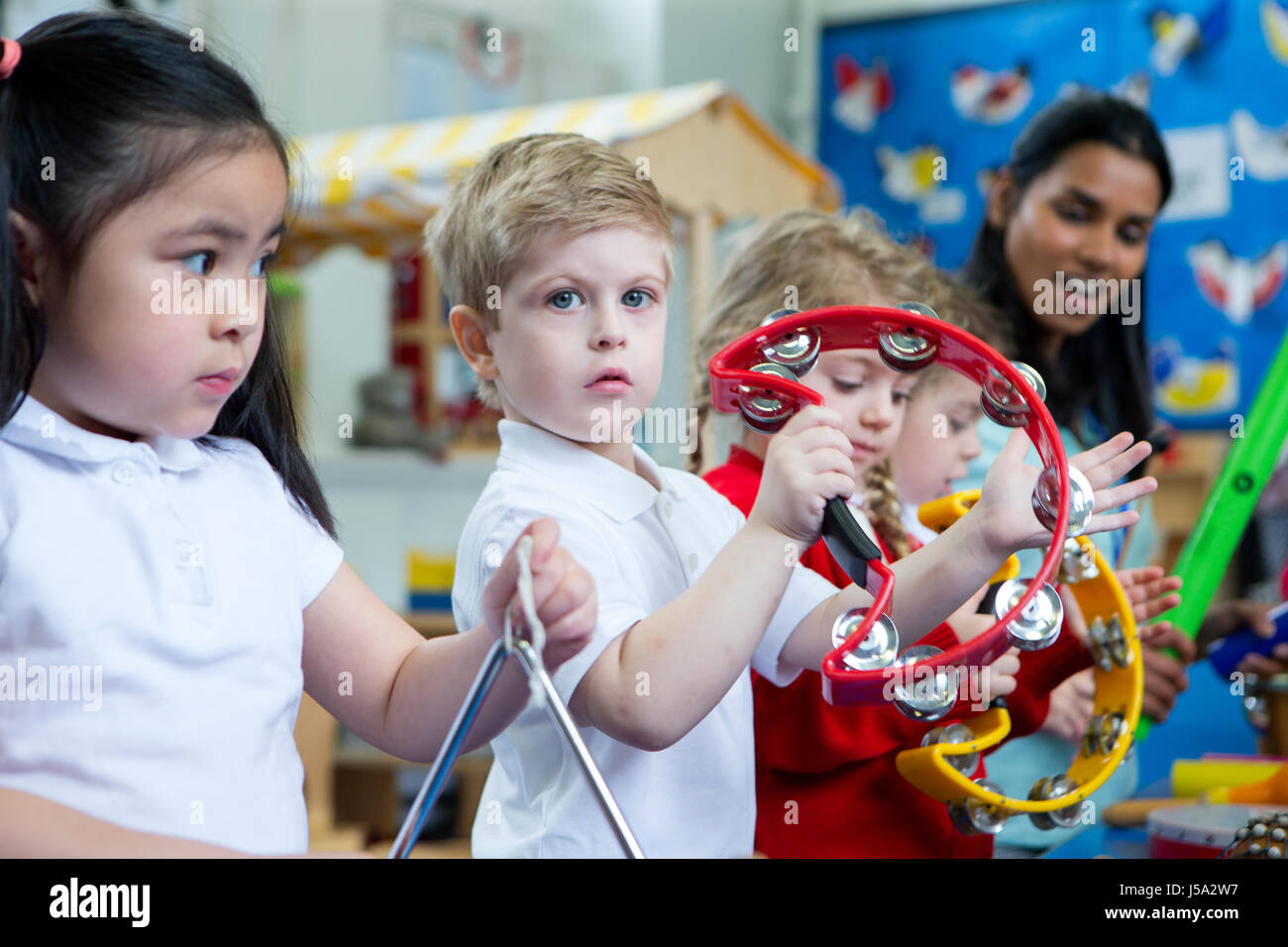 Jardin d'enfants jouant avec des instruments de musique en classe. Un petit garçon est à la recherche à l'appareil photo avec un tambourin. Banque D'Images