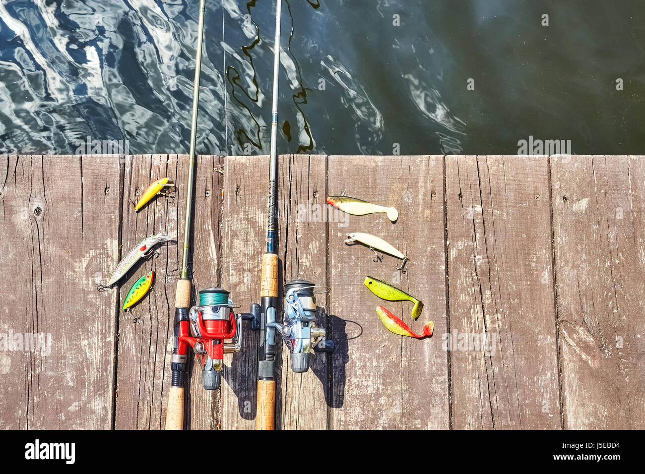 Deux cannes à pêche avec des moulinets et des leurres spinning artificiel sur une jetée en bois. Banque D'Images