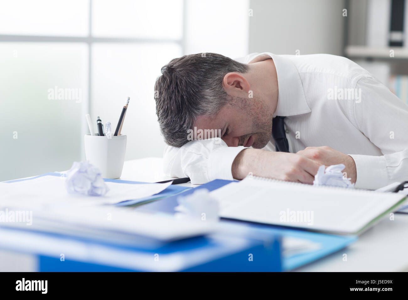 Épuisé businessman débordé par la paperasse, il est effondré et dormir sur son bureau, le stress et le surmenage concept Banque D'Images