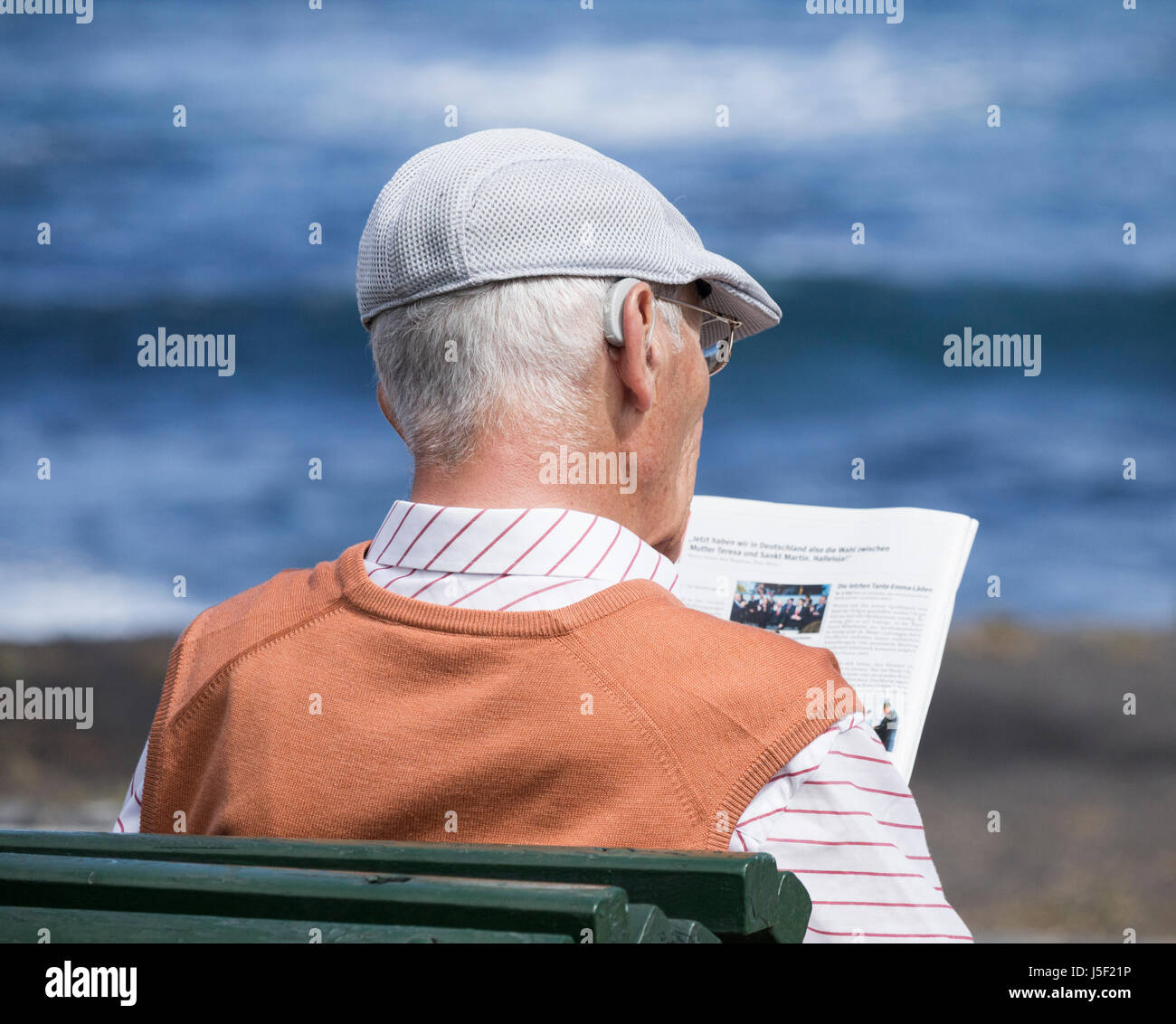 Un homme âgé portant une aide auditive lecture assis sur banc avec vue sur la mer. Banque D'Images