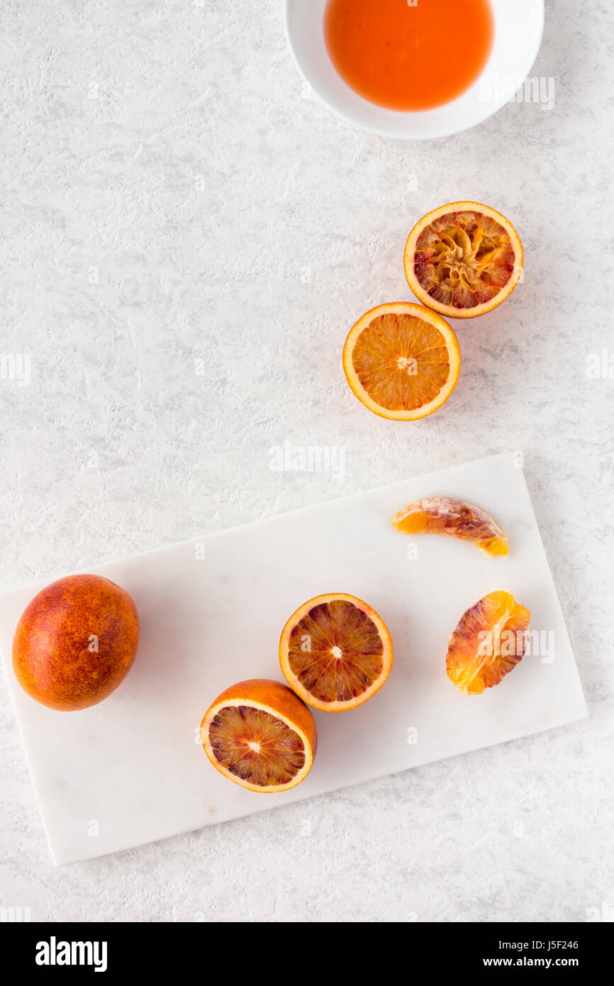 Ensemble, coupés en deux et pressé d'orange sanguine et de jus frais sur planche à découper et marbre blanc texturé Blanc fond marbré avec copie espace. Banque D'Images