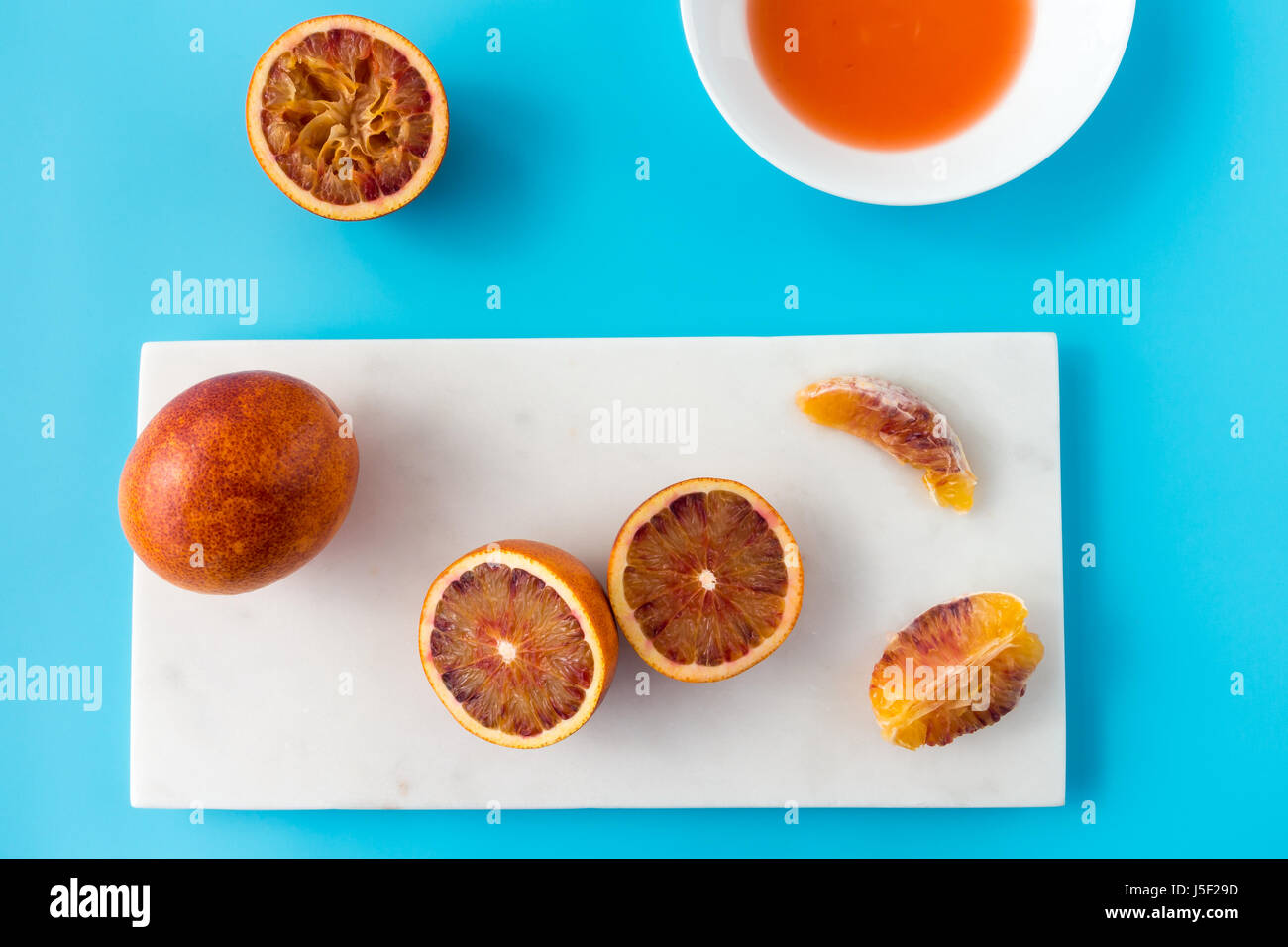 Ensemble, coupés en deux et pressé d'orange sanguine et de jus frais sur le marbre blanc planche à hacher et solide fond bleu. Banque D'Images