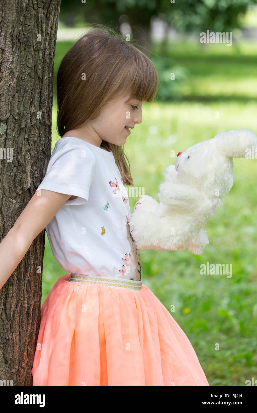 La petite fille appuyé contre un arbre tenant sa peluche préférée Banque D'Images
