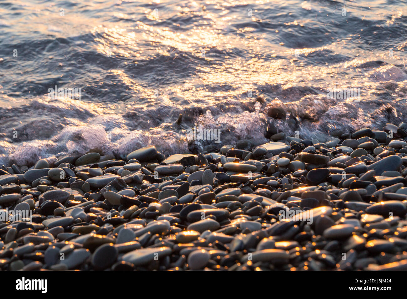 Brillant humide des pierres et petite vague sur le coucher du soleil sur la plage. Vue rapprochée. Banque D'Images