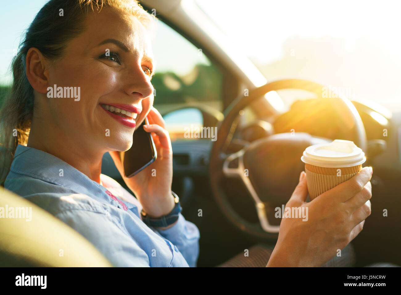 Young businesswoman parle sur le smartphone et de boire du café tout en conduisant une voiture Banque D'Images