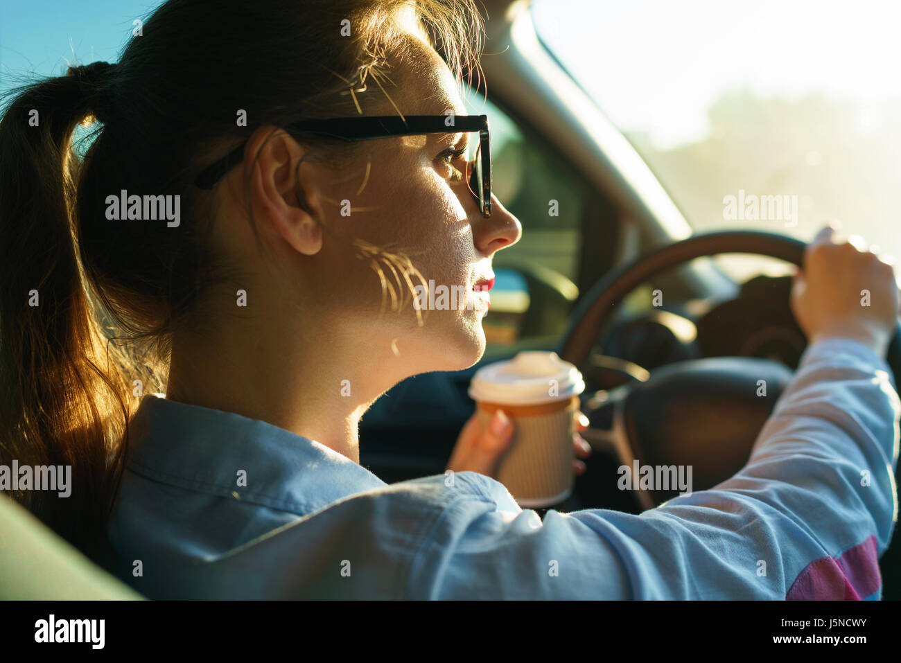 Jeune femme avec du café pour aller conduire sa voiture Banque D'Images