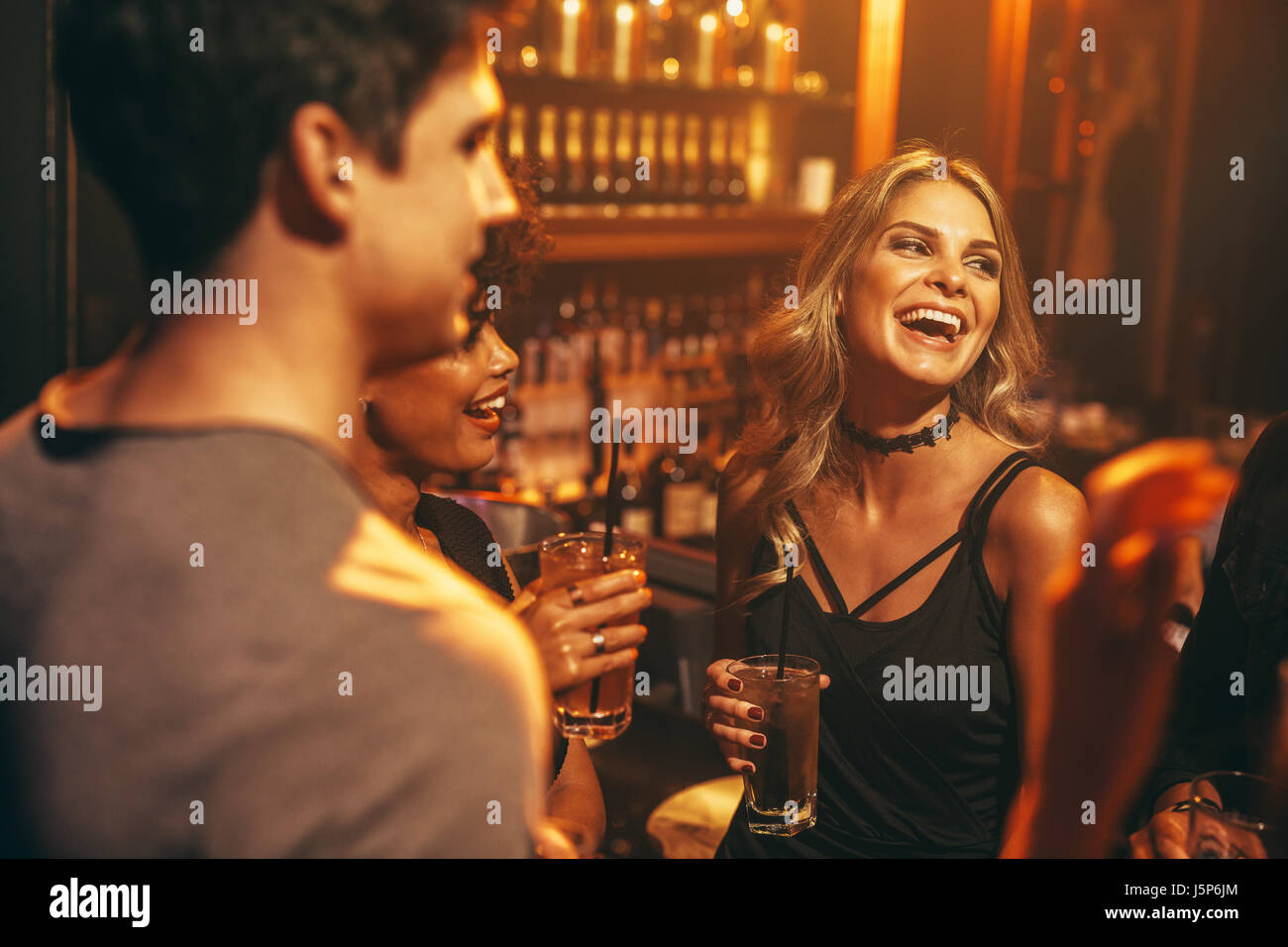 Belle jeune femme ayant un verre dans une discothèque avec des amis. Groupe de personnes appréciant partie dans un pub. Banque D'Images