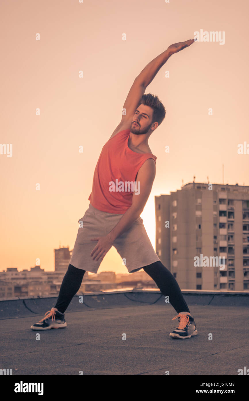 Un jeune homme adulte seulement, Lever coucher Soleil, s'étend le haut du corps, bras, s'étendant sur le toit du pavillon, les bâtiments derrière city Banque D'Images