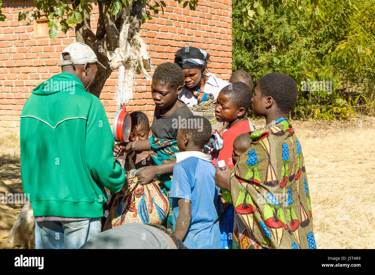 La vente d'enfants pesés sur les balances de maïs suspendu à arbre dans un village rural au Malawi, l'Afrique Banque D'Images