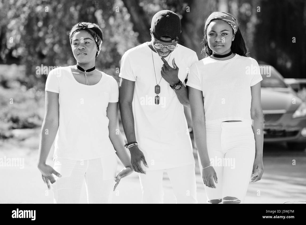 Trois amis américains de l'Afrique de l'élégant, l'usure des vêtements blancs contre rouges de luxe voiture de sport. Mode de rue de jeunes noirs. Un homme noir avec deux Banque D'Images