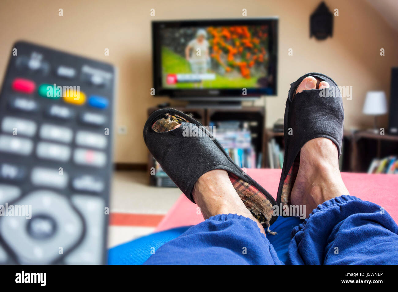 Télécommande et pomme de terre de divan, paresseux dans une chaise confortable portant des chaussons usés avec grands orteils dépasse et regarder la télévision dans la salle de séjour Banque D'Images