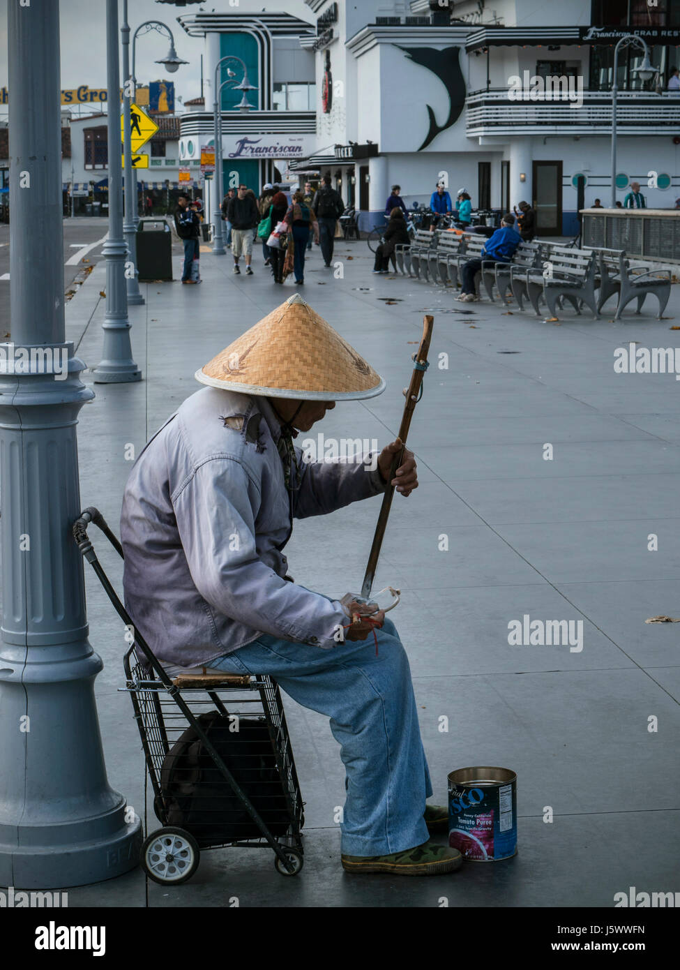 Busker mâle oriental wearing straw coolie hat et la lecture d'un Erhu, Le violon chinois chaîne deux sur le trottoir humide pour les trucs à la tombée de la Jetée 39 Embarcadero San Francisco California USA Banque D'Images