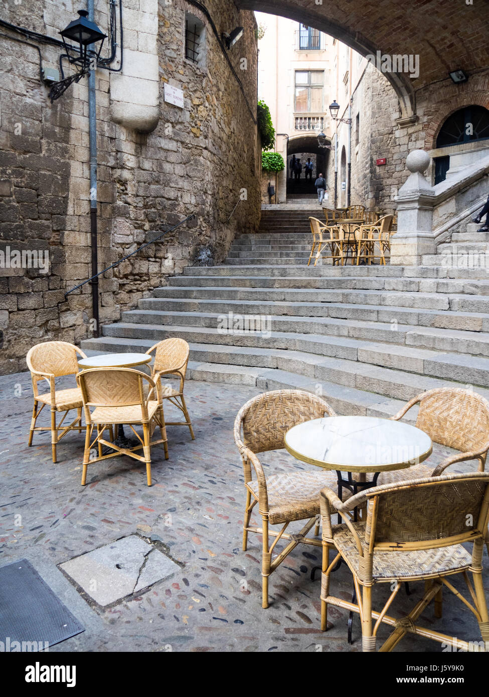Tables et chaises en rotin mis en place pour manger en plein air au pied de l'escalier de Sant Domènec, Pujada de Gérone, Espagne. Banque D'Images