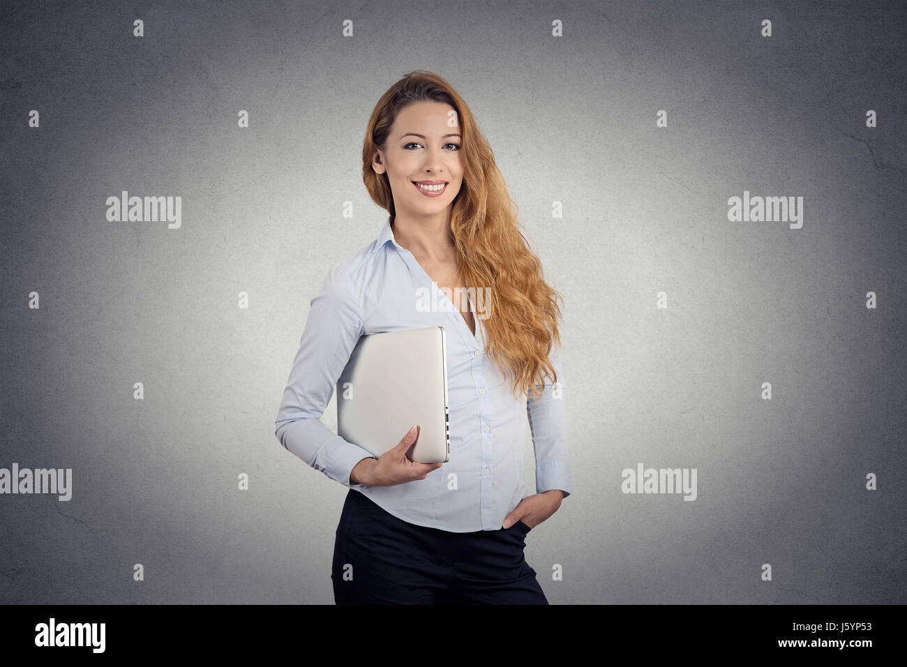 Portrait young beautiful happy woman holding laptop smiling standing bureau isolé sur fond de mur gris. Expression visage positif de l'émotion. Comput Banque D'Images