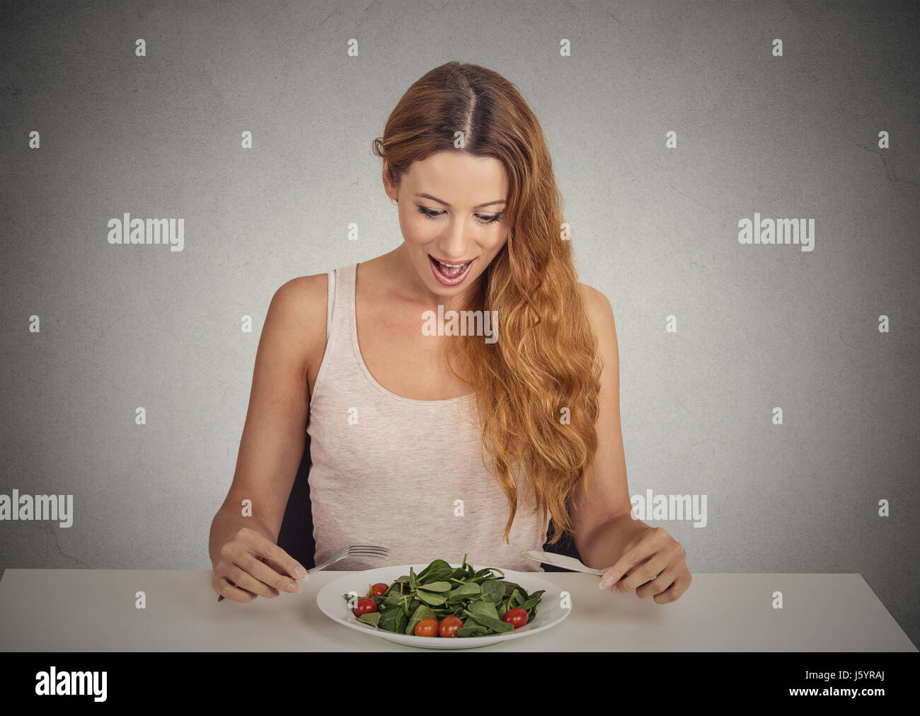 Portrait of attractive young woman eating salade verte isolée sur fond de mur gris studio shot. Régime de nourriture frais sain nutrition concept Banque D'Images