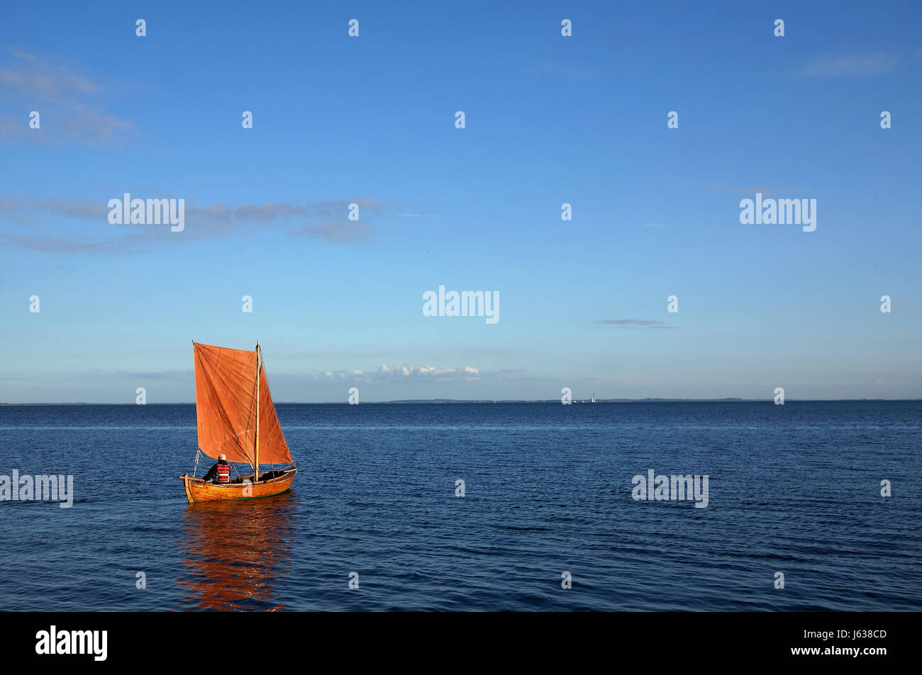 Petit bateau en bois avec voile orange et personne anonyme qui contrôle le bateau sur l'océan calme Banque D'Images