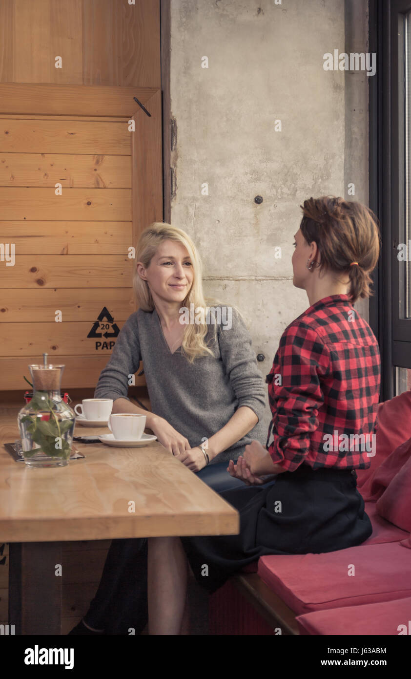 Les jeunes adultes, deux femmes parler assis, café-restaurant à l'intérieur, lumière du jour, jour ensoleillé café Banque D'Images