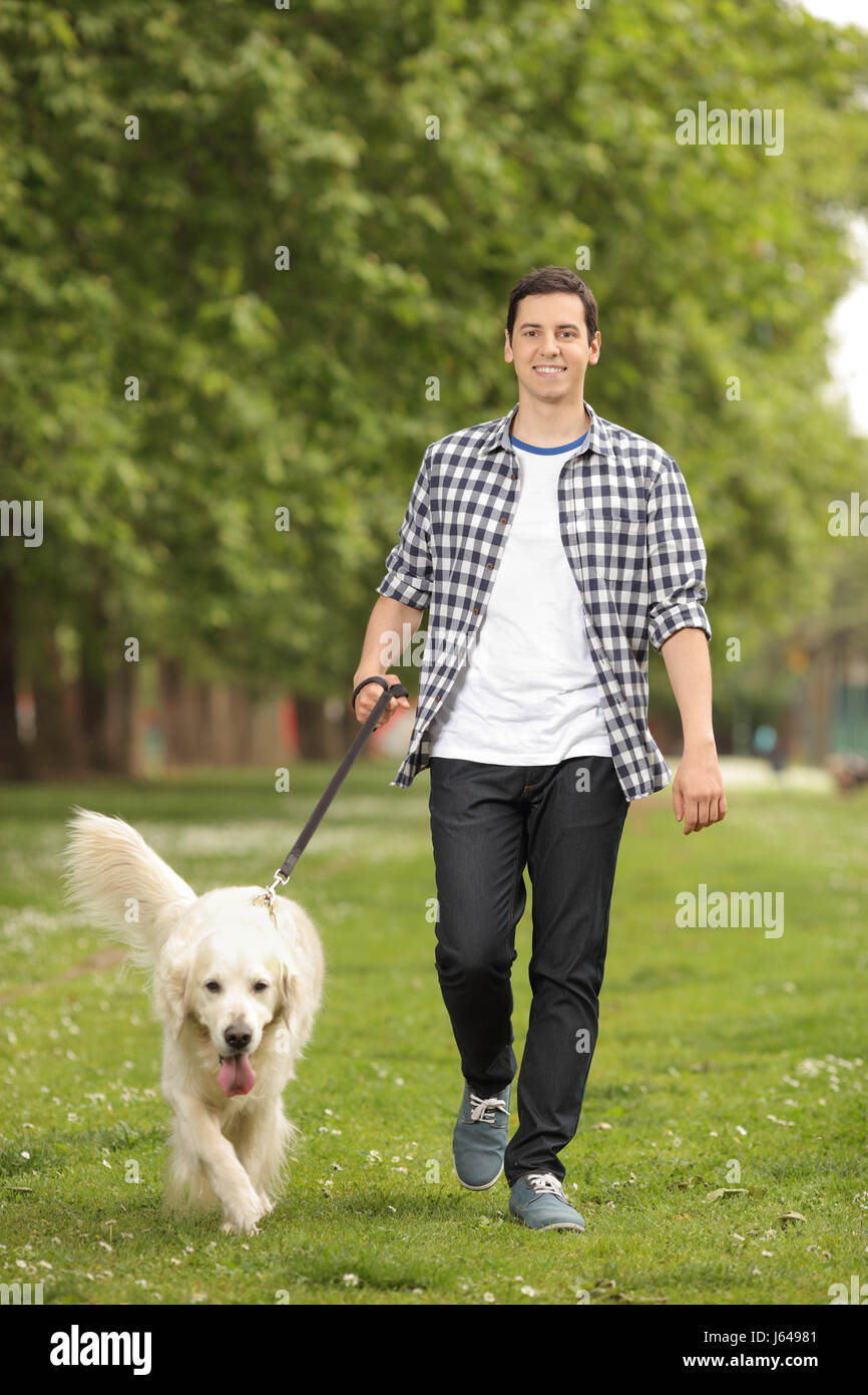 Portrait d'un jeune homme avec un chien à marcher en direction de la caméra dans un parc Banque D'Images