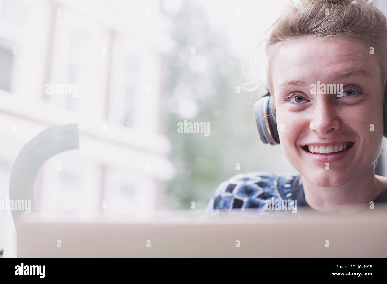 Portrait of smiling young woman wearing headphones at laptop dans fenêtre cafe Banque D'Images