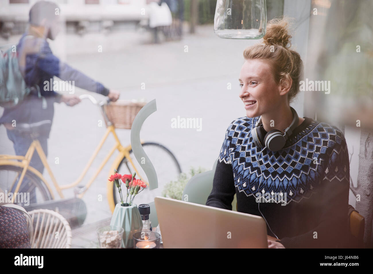 Smiling young woman using laptop in urban cafe window Banque D'Images