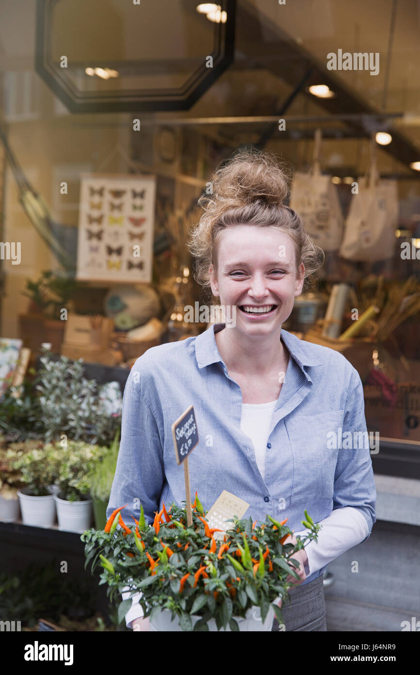 Portrait of smiling female florist holding potted plant at storefront Banque D'Images