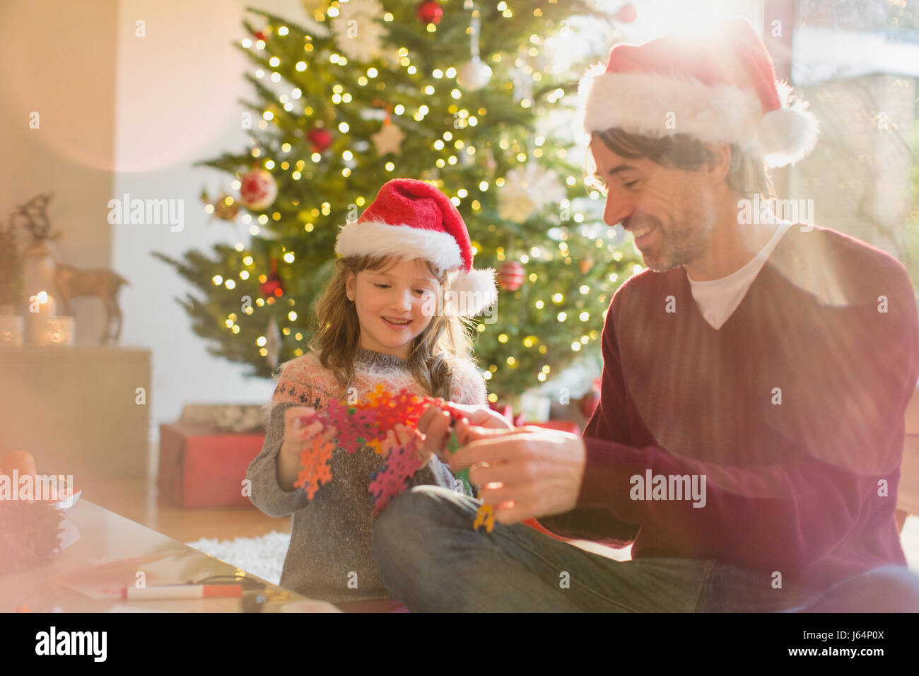 Père et fille wearing Santa hats et holding paper snowflakes near Christmas Tree Banque D'Images