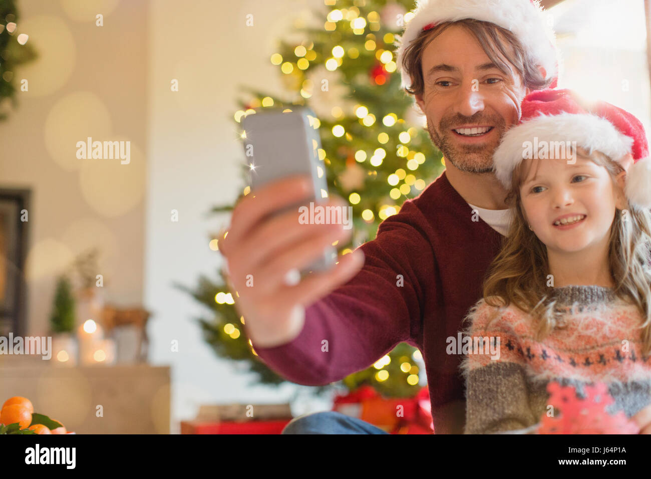 Père et fille souriante dans Santa hats en tenant avec selfies téléphone appareil photo Banque D'Images