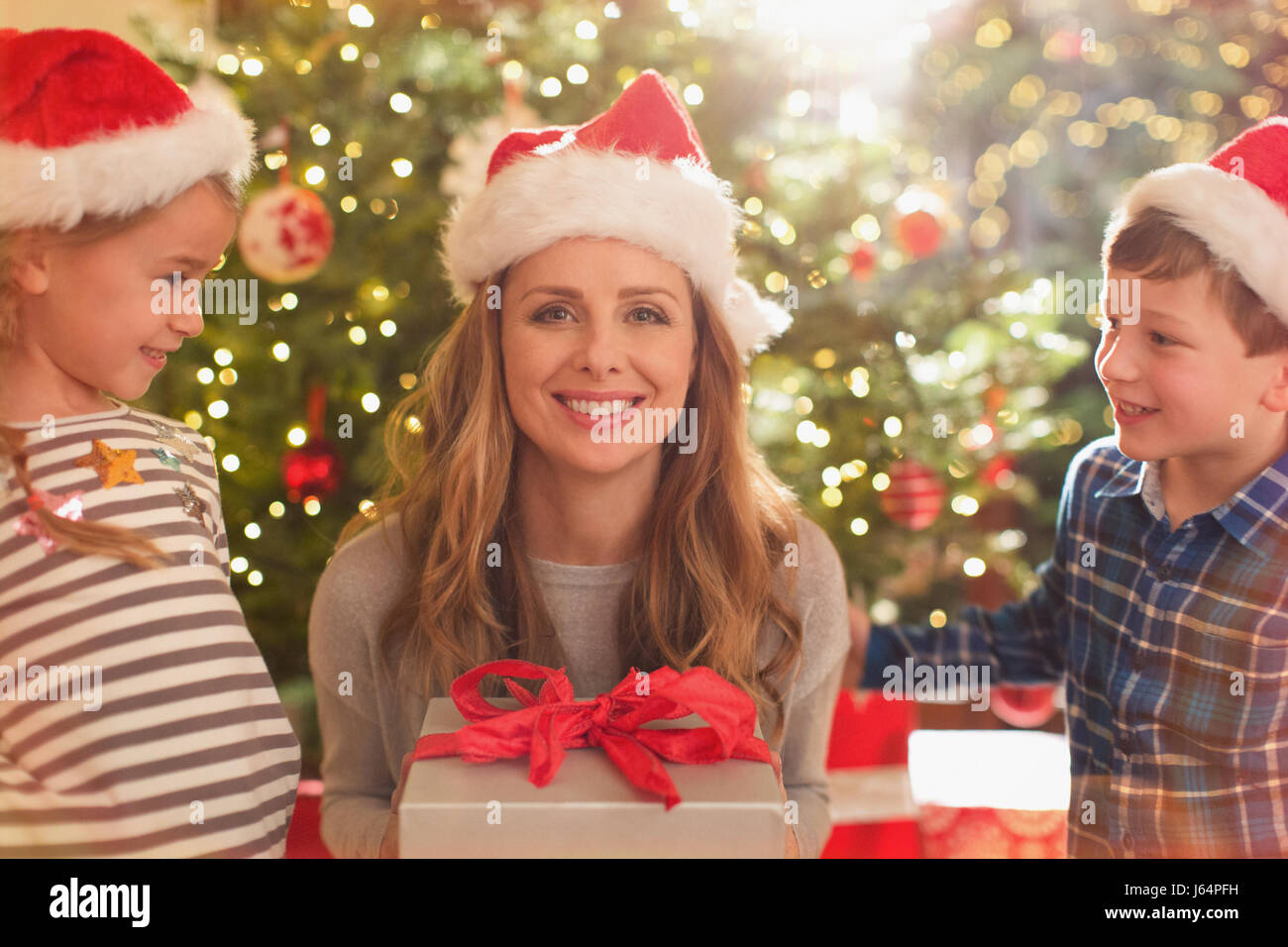 Portrait of smiling mother in Santa hat recevoir cadeau de Noël fille et fils Banque D'Images