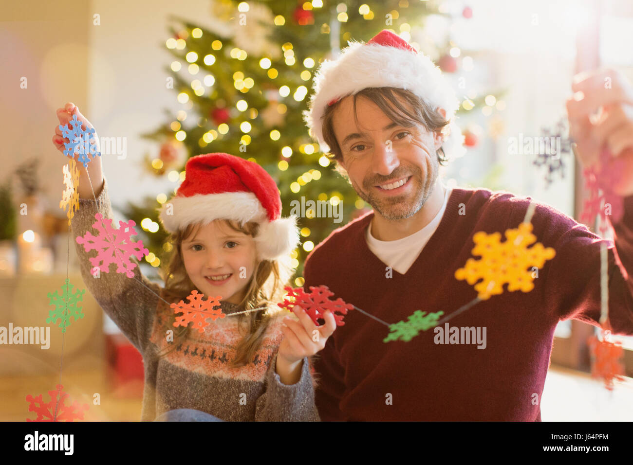 Portrait smiling père et fille dans Santa hats holding string de flocons de papier Banque D'Images