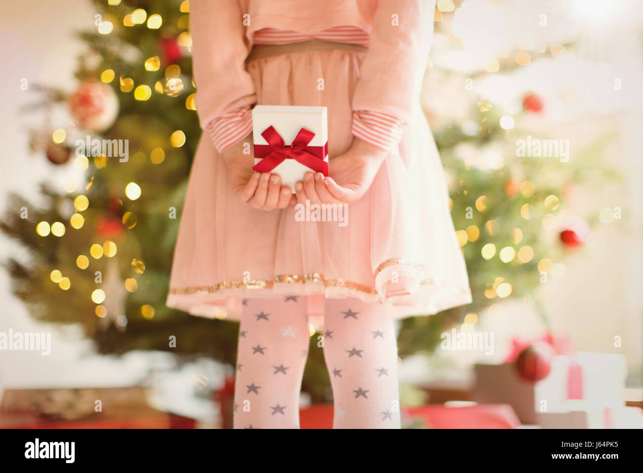 Fille en robe rose avec un cadeau derrière back in front of Christmas Tree Banque D'Images