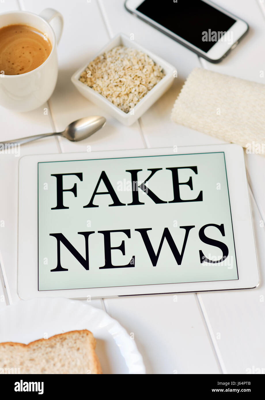 Libre d'un ordinateur tablette avec le texte de fausses nouvelles dans l'écran sur un tableau blanc pour le petit-déjeuner ensemble, avec un peu de céréales, une tasse de café et quelques chrit Banque D'Images