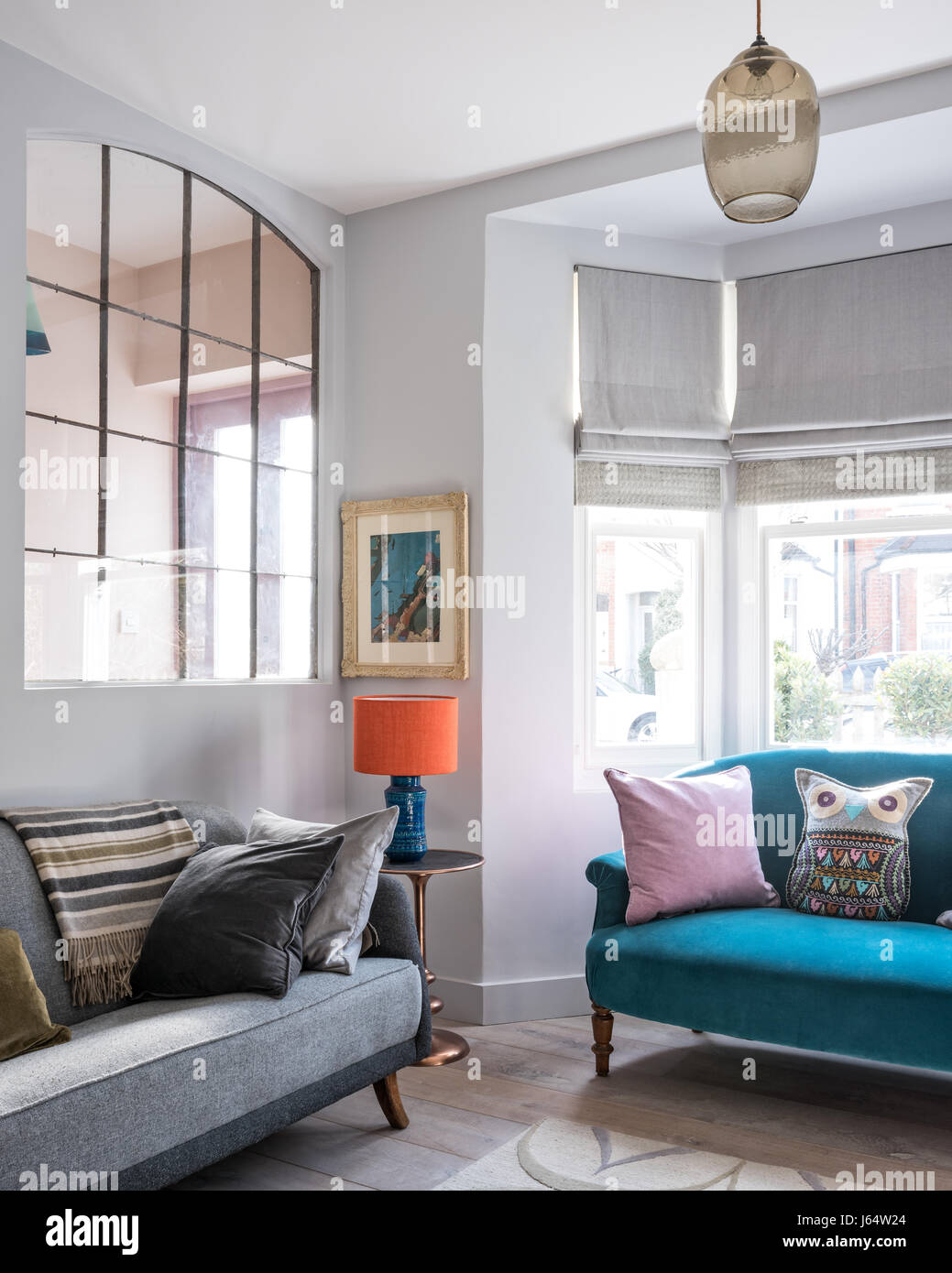 De grandes portes-fenêtres en métal récupéré dans la salle de séjour avec canapé vintage gris de Youssoupha. Le tapis est par Allegra Hicks et le petit canapé upholste Banque D'Images