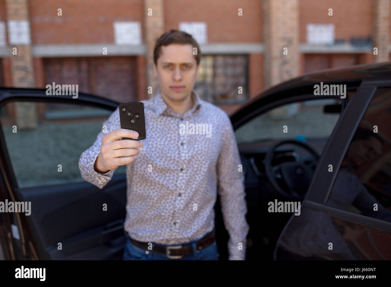 Jeune propriétaire homme debout près d'une voiture et la tenue d'une touche d'alarme de voiture. Effet de flou de l'homme. Banque D'Images