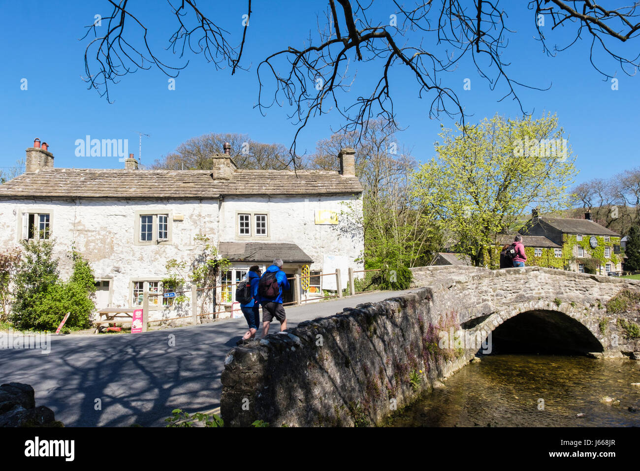 Les randonneurs à pied sur le vieux pont au-dessus de Malham Beck. Malham, Malhamdale, Yorkshire Dales National Park, North Yorkshire, Angleterre, Royaume-Uni, Angleterre Banque D'Images
