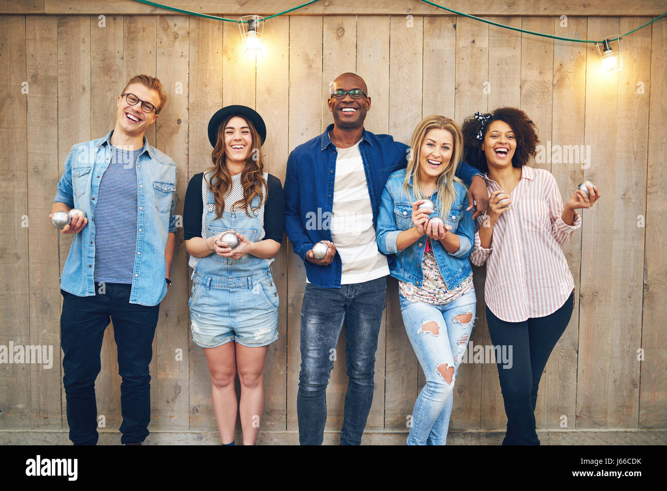 Joyeux groupe d'amis en noir et blanc au mur en bois debout avec des boules de pétanque et sourire ensemble. Banque D'Images