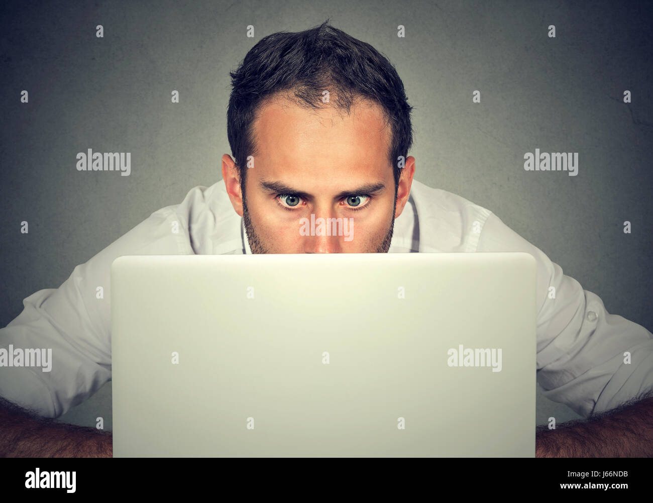 L'homme avec de grands yeux surpris de se cacher derrière un ordinateur portable à regarder l'écran avec une expression choquée face peur Banque D'Images