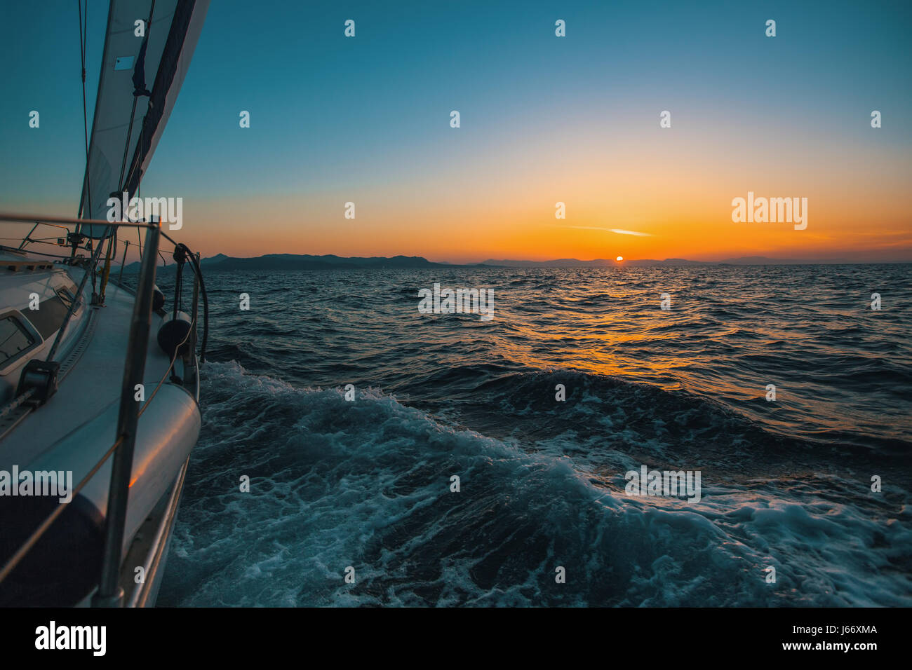 Yacht à voile à la glisse à travers les vagues de la mer lors d'un coucher de soleil magique. Banque D'Images