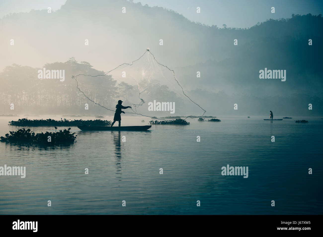 Le pêcheur son filet de pêche dans la rivière en le jetant en l'air élevé tôt le matin pour attraper de couleur bleu avec son petit poisson Banque D'Images