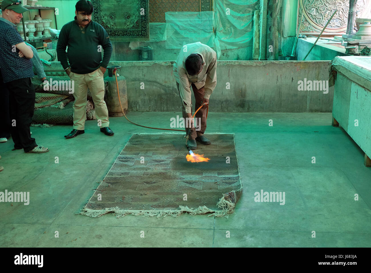 Artisan indien à l'aide d'un chalumeau pour brûler l'arrière d'un tapis noués à la main dans la région de Jaipur, Rajasthan, Inde Banque D'Images
