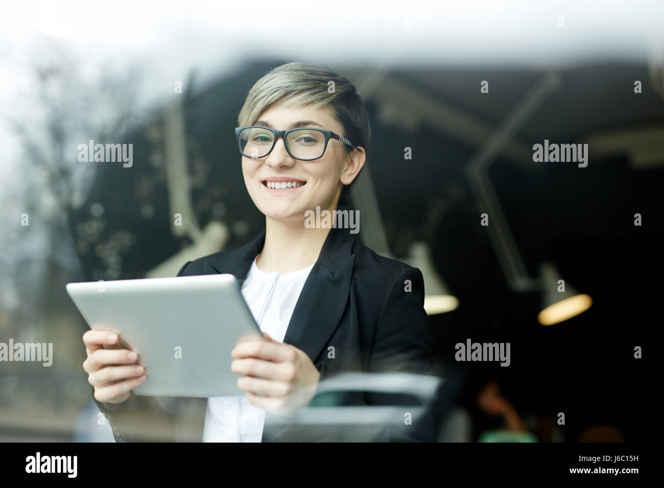 Portrait de jeune femme avec coupe de cheveux créatif et représentant de la génération Y, vitré, à l'aide de tablette numérique pour travailler en images à l'appareil photo Banque D'Images