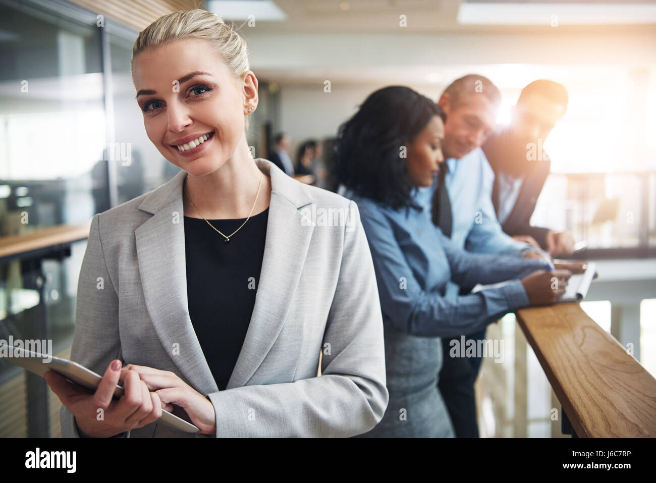 Smiling young blonde woman looking at camera d'affaires et de navigation tablet standing in office. Banque D'Images