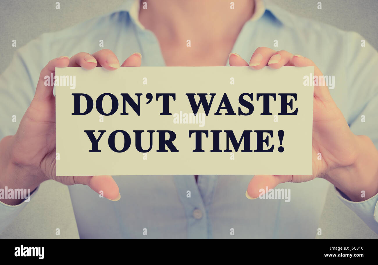 Young hands holding white card signe avec ne perdez pas votre temps message texte isolé sur fond de bureau mur gris. Retro style instagram amp Banque D'Images