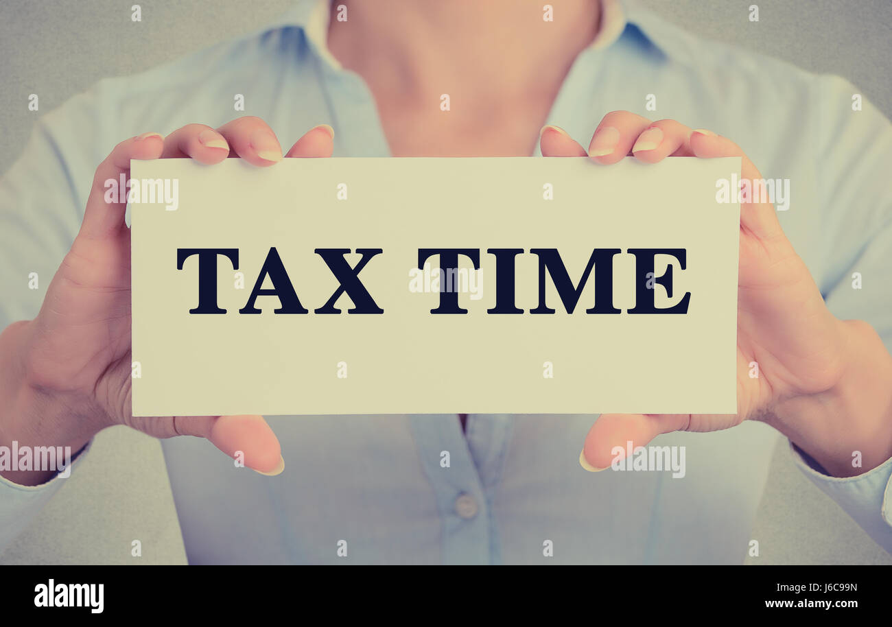 Libre de businesswoman hands holding white card signe avec temps d'impôts message texte isolé sur fond de bureau mur gris. Image retro style instagram Banque D'Images