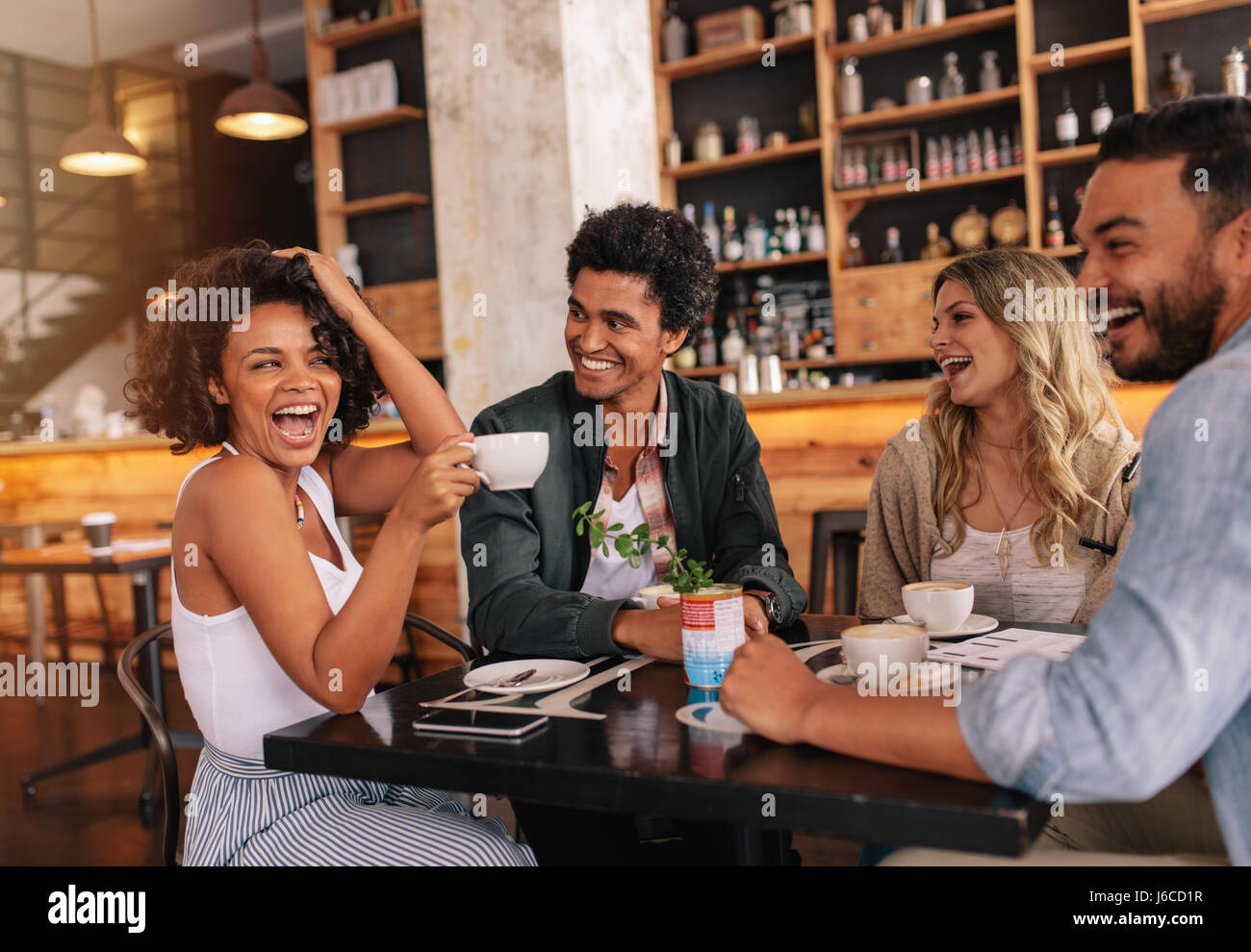 Heureux les jeunes gens assis autour de cafe table et boire du café. Groupe multiracial de friends enjoying coffee ensemble dans un restaurant. Banque D'Images