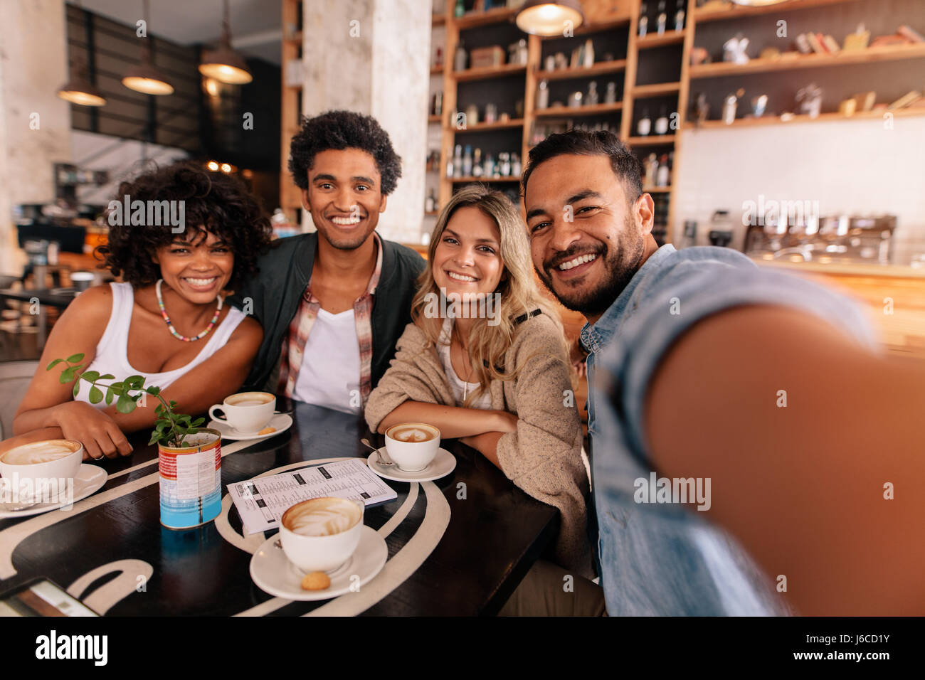 Heureux jeune homme en tenant avec des amis selfies dans un café. Les jeunes gens multiracial dans un café prendre un autoportrait. Banque D'Images